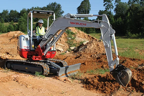 Operator trenching with Takeuchi TB225 compact excavator on a dirt construction site.