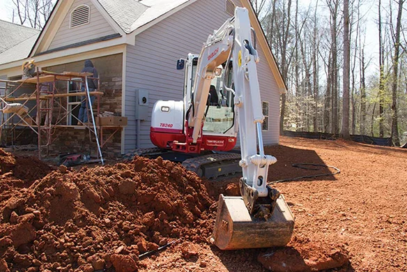 Takeuchi TB240 compact excavator digging foundation next to residential home.