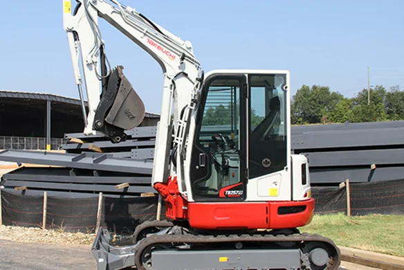 Takeuchi TB257FR compact excavator lifting bucket near metal construction materials.