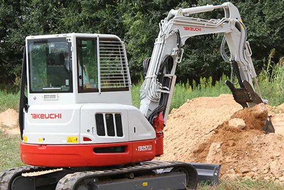 Takeuchi TB257FR mini excavator scooping dirt on a job site with trees in background.