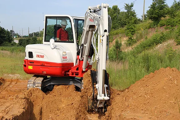 Takeuchi TB260 compact excavator trenching in dense clay soil on construction project.