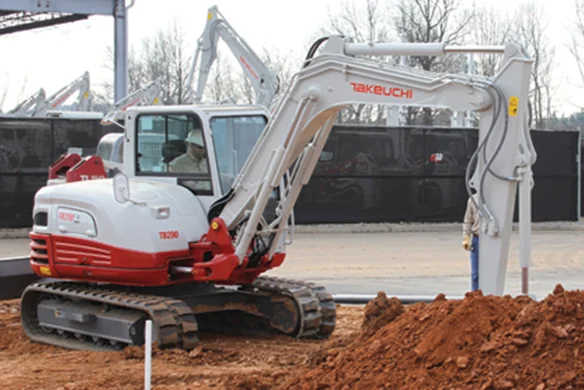 Operator using Takeuchi TB290 excavator for heavy-duty digging near gravel and pipework.