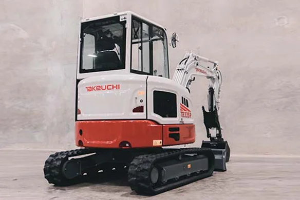 Rear view of a Takeuchi TB335R mini excavator indoors, showcasing its compact design and rubber tracks.