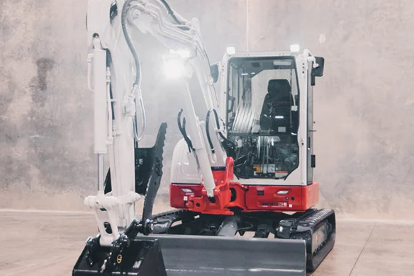 Takeuchi TB350R excavator with front blade and bucket extended, lit for display in a dealership showroom.