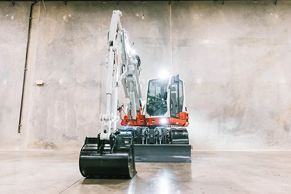 Front view of Takeuchi TB395W wheeled excavator with blade and boom, parked indoors.