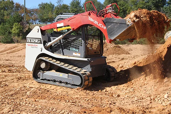 Side angle of Takeuchi TL12R2 track loader scooping dirt on a construction site.
