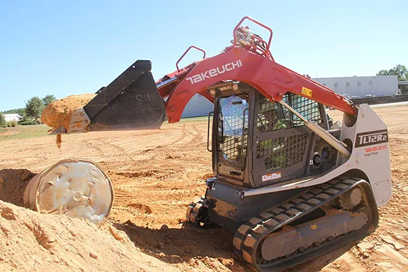 Takeuchi TL12R2 compact loader dumping dirt near metal drum on construction site.