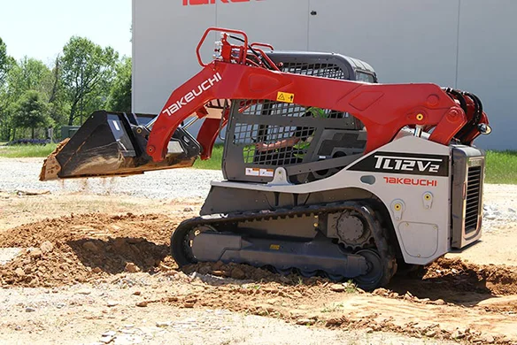 Takeuchi TL12V2 loader scooping soil at jobsite with vertical lift arms extended.