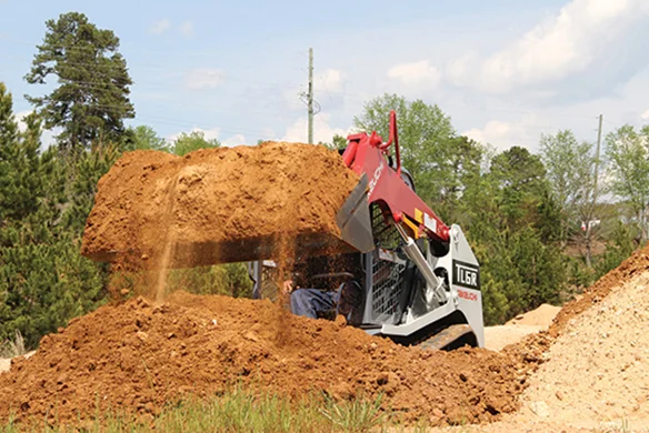 Takeuchi TL6R track loader lifting a large bucket of dirt at a construction site.