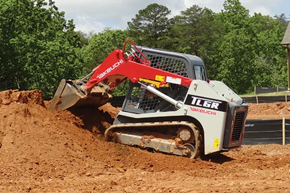 Takeuchi TL6R track loader moving dirt on job site, showcasing compact performance in earthmoving applications.