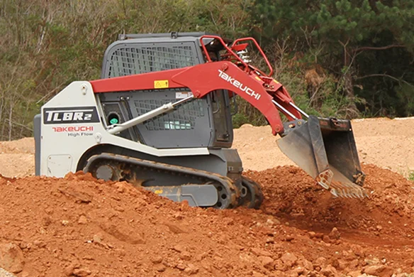 Takeuchi TLB2R2 high-flow compact loader digging into red clay soil, optimized for heavy-duty excavation.