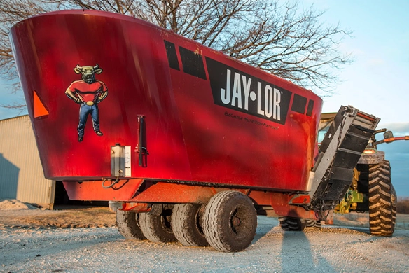 Close-up of Jaylor twin auger vertical feed mixer wagon attached to a tractor on a farm.