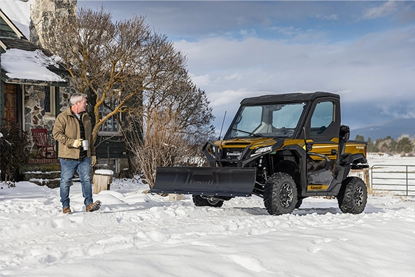 Yellow and black Kawasaki Ridge HVAC Limited Edition with snow plow attachment clearing a snowy driveway near a house.