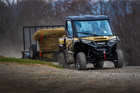 Side profile view of a gold and black Kawasaki Ridge HVAC Limited utility vehicle with enclosed cab, parked on a white background.