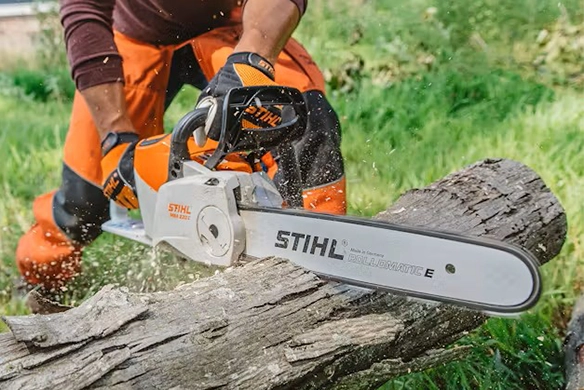 Close-up of Stihl chainsaw cutting through an old log on a green, grassy field.