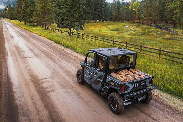 Rear 3/4 view of the Kawasaki Ridge XR Crew Limited, driving on a dirt road with a full load of chopped firewood in the cargo bed.