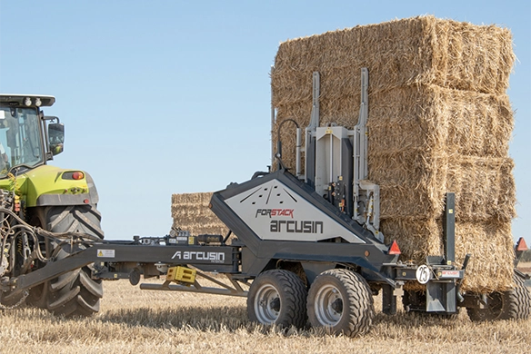 Close-up side view of the Arcusin Forstack system stacking a tall column of straw bales.