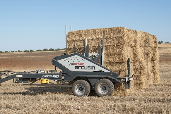 Arcusin bale accumulator loaded with a large stack of straw bales in a harvested field.