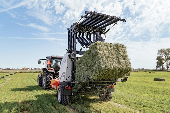Arcusin AutoStack bale bundler lifting green hay bales in a field with a tractor.