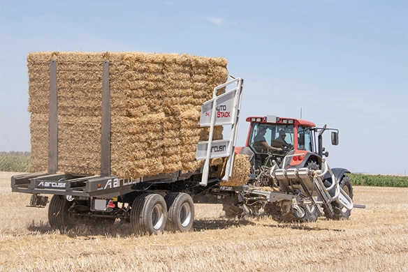 Arcusin AutoStack bale stacker collecting and loading straw bales onto a trailer towed by a red tractor.