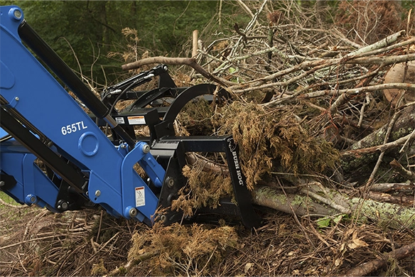 A blue 655TL front loader equipped with a construction grapple attachment, lifting a pile of brush and debris.