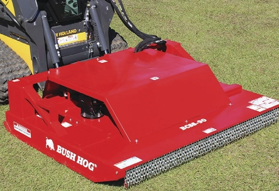 Bush Hog skid steer brush cutter attached to a New Holland loader on grass
