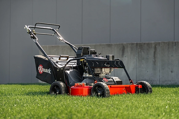 Exmark walk-behind mower parked on a bright green lawn with a concrete wall in the background.
