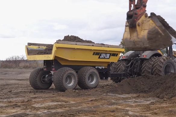 A Jaylor dump wagon being filled with soil on a construction site using an excavator.