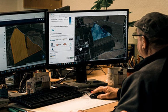 Farmer looking at computer screens containing data from PTx Trimble software solutions.