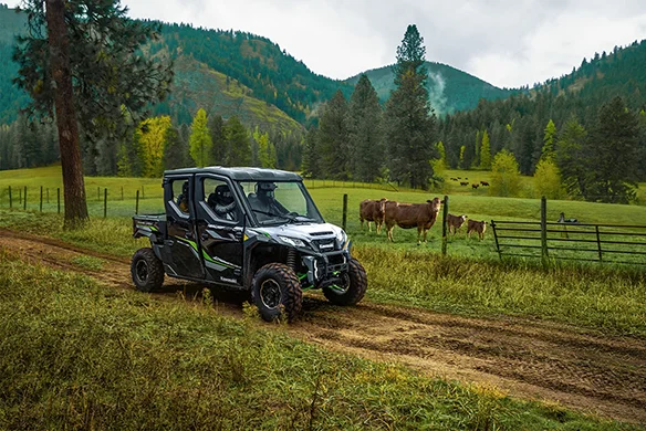 A Kawasaki Ridge XR Crew model parked in a forest stream while a group of people are fishing and exploring the area.