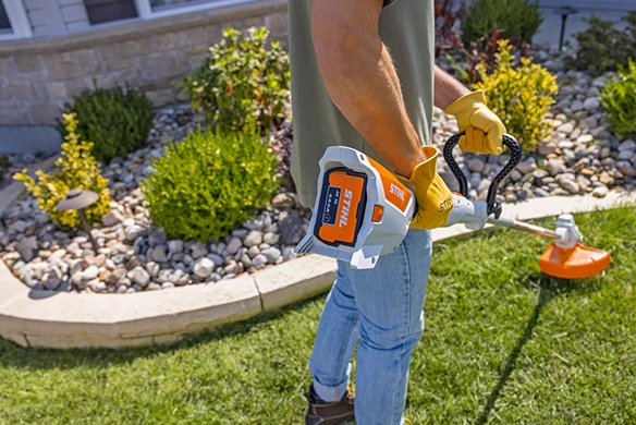 Man trimming lawn edges with a STIHL battery-powered trimmer near landscaped garden beds.