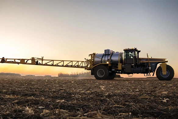 TerraGator liquid applicator spraying field at sunset with boom arms extended
