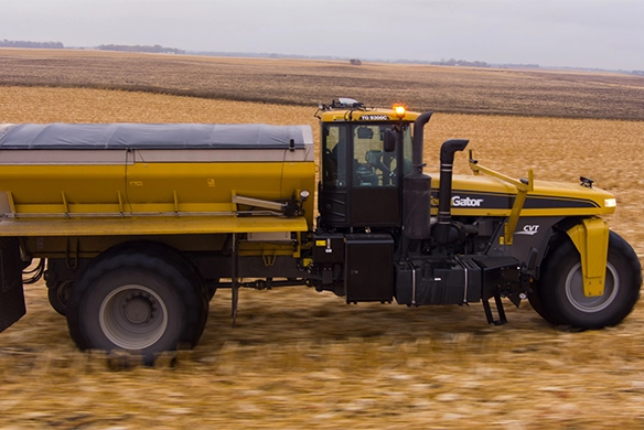 Side view of TerraGator dry spreader applying fertilizer in crop stubble field.