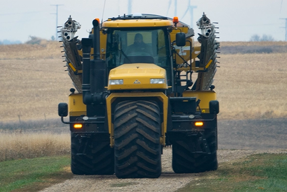 Front view of TerraGator dry spreader driving on a rural dirt path with applicator arms folded.