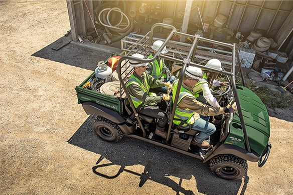 Overhead view of four workers in safety vests and helmets seated in a Kawasaki Mule 4010 Trans with tools loaded in the cargo bed.