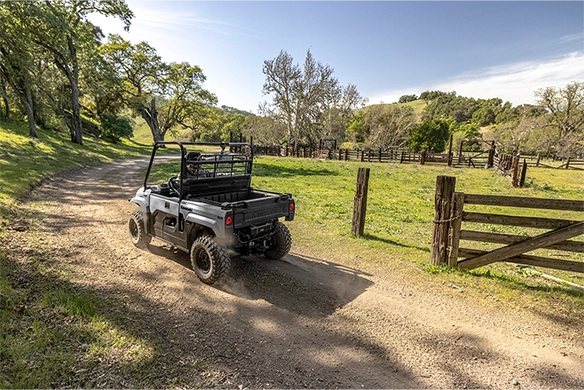 Rear view of a Kawasaki Mule PRO-MX driving down a tree-lined dirt path toward a livestock pen.
