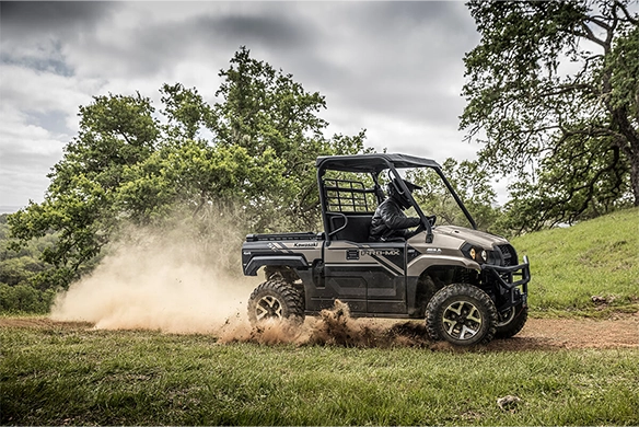 Side view of a black Kawasaki Mule PRO-MX SE kicking up dirt on a forest trail with a rider in motion.