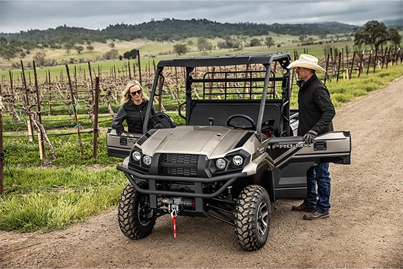 Front view of a black Kawasaki Mule PRO-MX SE parked near a vineyard, with two people preparing for work.