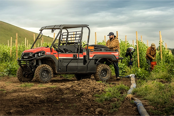 Workers harvest crops in a field while a red Kawasaki Mule PRO-FX1000 HD is parked nearby with irrigation pipes at its side.