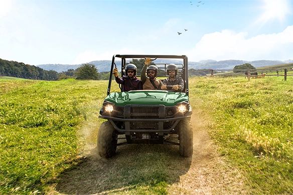 Three passengers ride a Kawasaki Mule PRO-FX 820 across a grassy field on a bright sunny day.