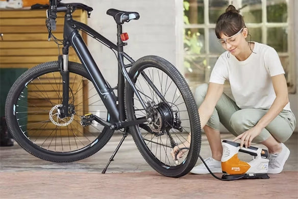 Woman using a STIHL portable air inflator to fill the tire of a bicycle inside a sunlit garage.