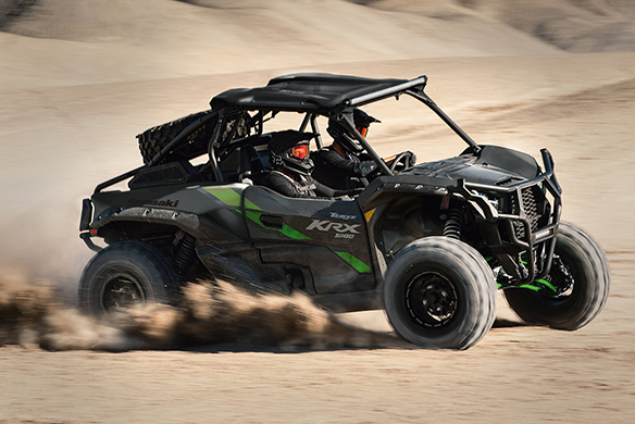 Riders enjoying a Kawasaki Teryx KRX 1000 side-by-side on sand dunes.
