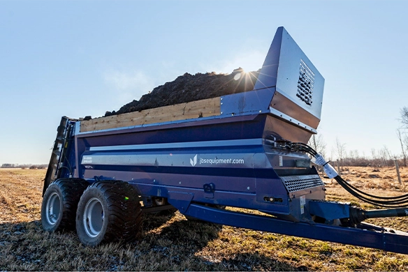 JBS manure spreader loaded with material in a field, highlighting its high-capacity build and rugged construction