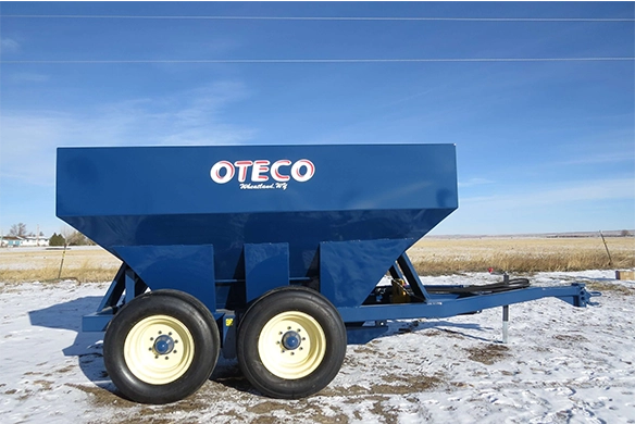 OTECO grain or feed cart with twin axles and heavy-duty frame, parked in a snowy field under a clear sky