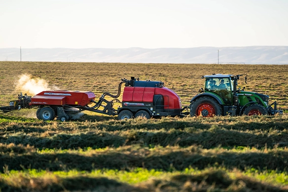 Staheli West DewPoint 632 steam application system in operation between a baler and tractor, optimizing hay moisture.