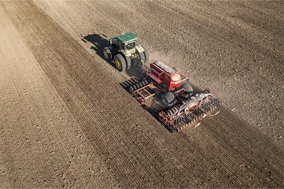 John Deere tractor operating a Horsch seed drill system across a freshly tilled field during planting.