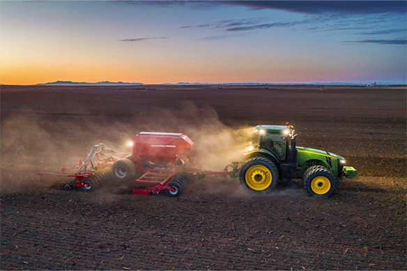 John Deere tractor pulling a Horsch seeding system through a dusty field during early evening operation.