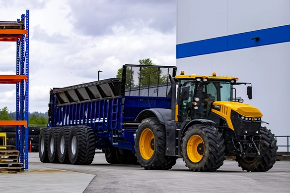 Large JBS Low-Rider manure spreader attached to a tractor, parked outside a commercial ag facility.