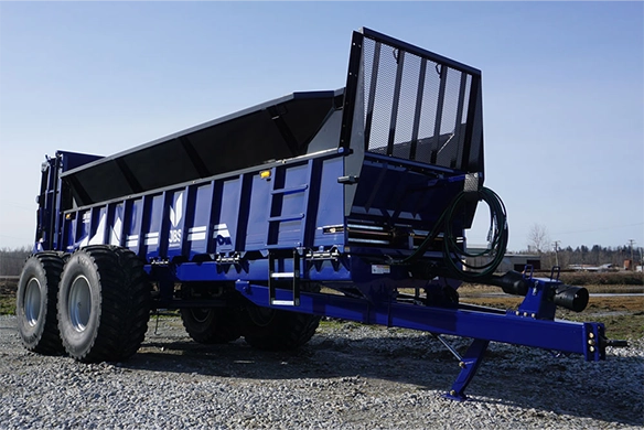 JBS Low-Rider manure spreader on gravel, showcasing wide flotation tires and robust frame design.