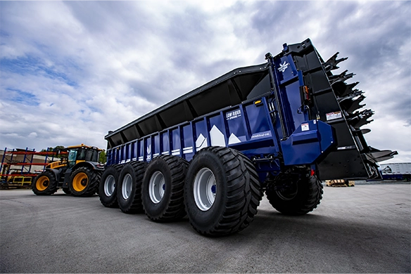 Rear angle of JBS Low-Rider spreader, showing multiple axles and rear discharge system under cloudy skies.